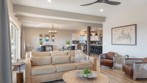 Ein geräumiges Wohnzimmer mit einem beigen Sofa, einem Couchtisch und Ledersesseln. Im Hintergrund ist ein Essbereich mit Tisch und Stühlen zu sehen.