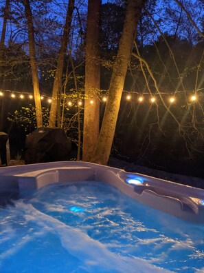 A hot tub surrounded by trees with string lights.