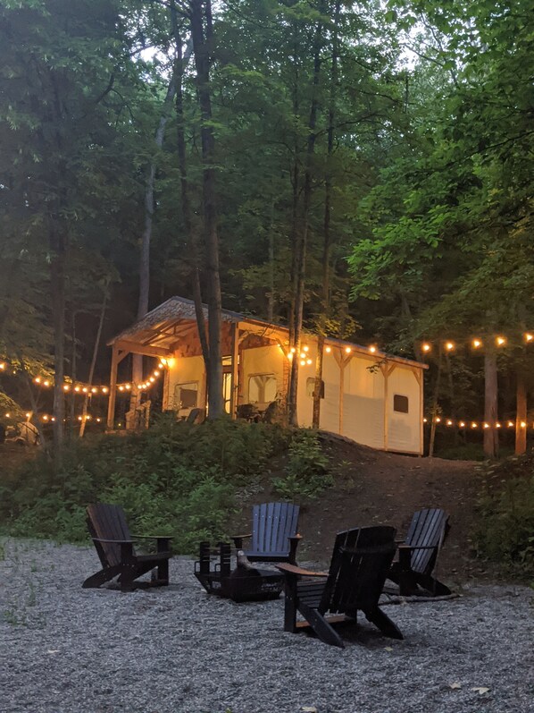 A rustic cabin with string lights, surrounded by trees, and outdoor seating.