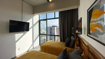 Habitación de hotel con dos camas, televisión de pantalla plana, ventana grande con vista a la ciudad y ventilador de techo.