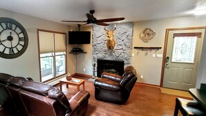A living room with leather sofas, a fireplace, a mounted deer head, a clock, and a television.