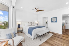 Ein modernes Schlafzimmer mit einem großen Bett, einer Bank, einem Deckenventilator und Blick ins Freie.