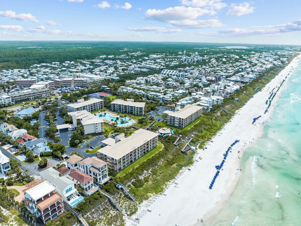 Vista aérea de una zona residencial costera con acceso directo a la playa, destacando un gran complejo hotelero con varias construcciones, una piscina y una playa con sombrillas.