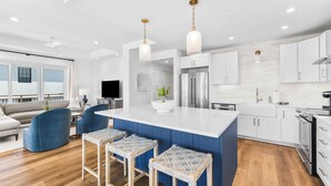 Una cocina moderna con armarios blancos, un refrigerador de acero inoxidable y una isla azul con taburetes de bar.