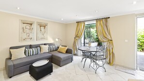 A living room with a grey sectional sofa, a round metal table, and yellow curtains. - 3-room apartment with private pool (in season) and garden (Antibes)