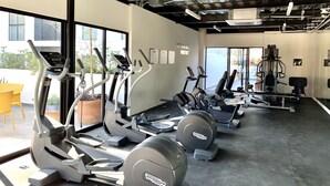 Un gimnasio con diferentes equipos de ejercicio, ventanas amplias y vistas al exterior.