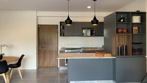 Una cocina moderna con una isla central, iluminación colgante y estanterías empotradas.