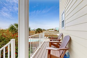 Una terraza de madera con dos sillas Adirondack, una piscina y vista a la playa y al océano.