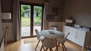 Eine moderne Küche mit weißen Schränken, einem Esstisch mit Stühlen, einem großen Fenster mit Vorhängen und einem flachbildfernseher, der über der Arbeitsplatte angebracht ist.