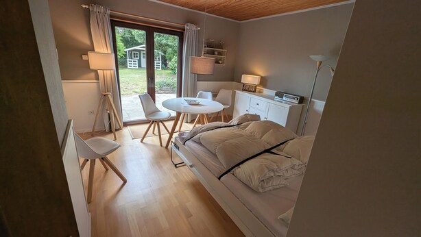 Ein Schlafzimmer mit Bett, Schreibtisch, Stühlen und Blick ins Freie.