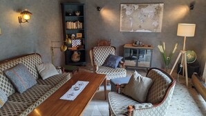Ein gemütliches Wohnzimmer mit Sofa, Sessel und Couchtisch. Ein Bücherregal, ein Globus und eine Lampe sind ebenfalls vorhanden.