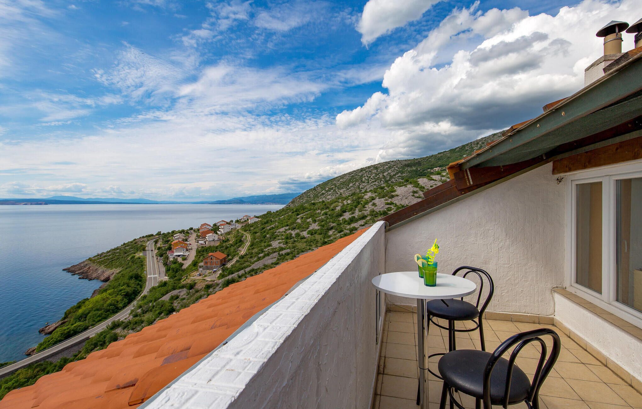 Un balcon avec une table et des chaises donnant sur un village côtier et la mer.