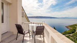 Un balcón con dos sillas y una mesa, con vista a un lago tranquilo y montañas lejanas.