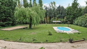Ein Garten mit Schwimmbad, Tennisplatz und überdachter Sitzgelegenheit.