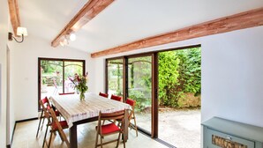 Ein Essbereich mit einem Holztisch, roten Stühlen und einem Blumenstrauß. Große Fenster bieten Blick auf Grünfläche.