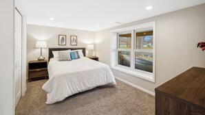 A bedroom with a large bed, two bedside tables with lamps, a window with a view, and a door. - Brand New WATERFRONT Listing! (Bloomington)