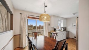 A modern kitchen with white cabinets, a wooden dining table, and a hanging light fixture. - Brand New WATERFRONT Listing! (Bloomington)