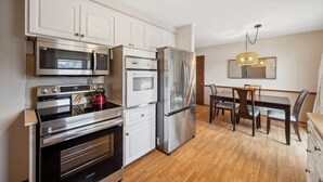 A modern kitchen with stainless steel appliances, a dining area with wooden furniture, and a chandelier. - Brand New WATERFRONT Listing! (Bloomington)