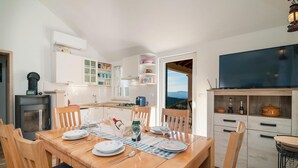 A modern kitchen with white cabinets, a built-in stove, and a dining area with a wooden table set for four. - Beautiful home in Postira (Postira)
