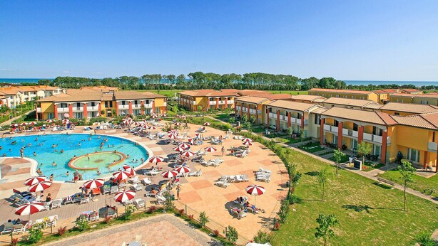 Een resort met een centraal gelegen zwembad, diverse zonnedekken en uitzicht op zee.