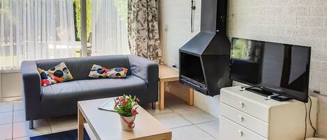Una sala de estar con un sofá, una mesa de centro, un televisor, una chimenea y un pequeño armario blanco.