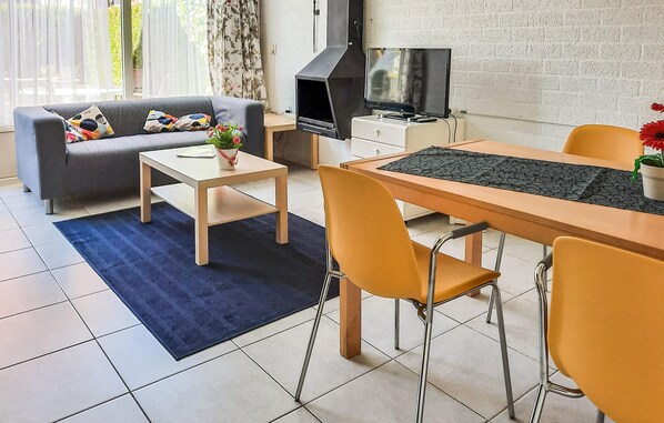 Un salon moderne comprenant un canapé, une table basse, une table à manger et des chaises. On y trouve également un téléviseur, une cheminée et une fenêtre avec des rideaux.