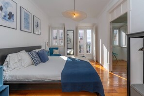 A bedroom with a bed, a blue chair, a large window, and a door leading to another room.