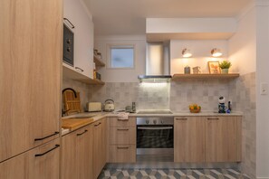 A compact kitchen with wooden cabinets, a built-in oven, a window, and a countertop with various items.