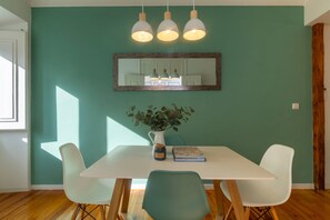 A dining area with a white table, four chairs, a vase with a plant, and a mirror above the table.