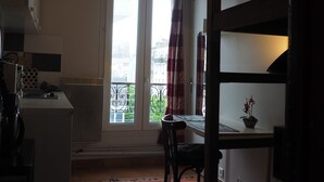 A compact kitchen with a washing machine, a dining table with a chair, and a view of the city through a window with curtains. - Beau Studio Bien Équipé (Le Pré-Saint-Gervais)