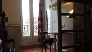 A room with a dining table, chairs, a radiator, a window with curtains, and a view of buildings outside. - Beau Studio Bien Équipé (Le Pré-Saint-Gervais)
