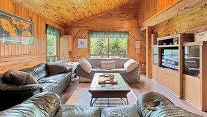 Ein gemütliches Blockhaus-Interieur mit Holzwänden, einem Deckenventilator, einem Essbereich und einem Fernseher, der eine Speisekarte zeigt.