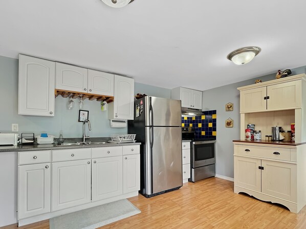 A modern kitchen with white cabinets, stainless steel appliances, and a wooden floor.