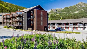 Ein modernes Hotel mit mehreren Etagen, einem Parkplatz und einer Bergkulisse.