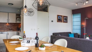 A modern kitchen with a dining area, featuring a wooden table set for a meal, a wine bottle, and a clock on the wall.