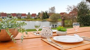 A wooden table set for a meal with a view of a lake and houses in the background.