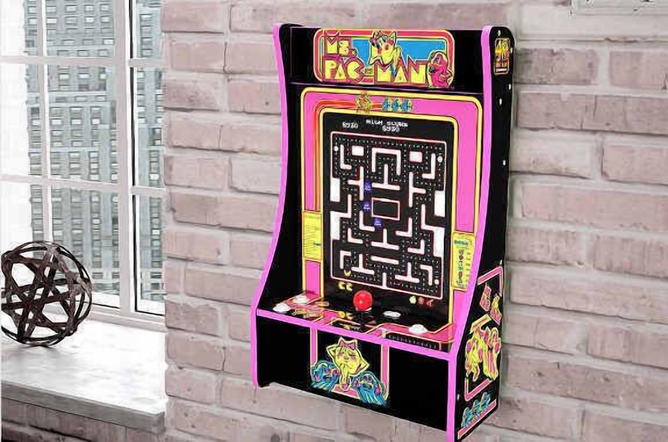 A Pac-Man arcade machine mounted on a brick wall.