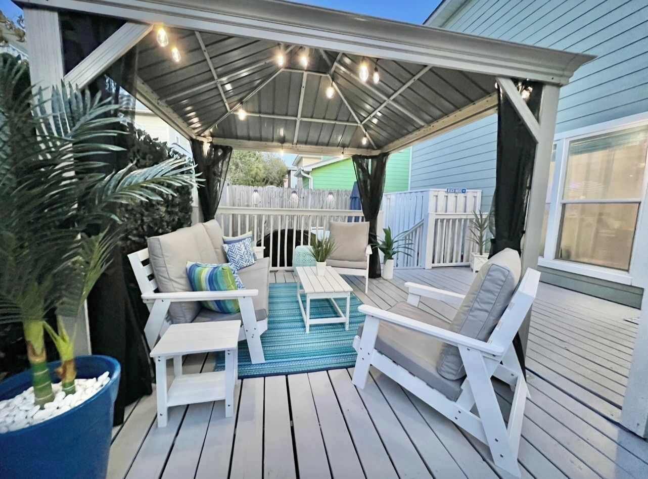 Een terras buiten met witte meubels, een overdekt gedeelte en een blauw vloerkleed.