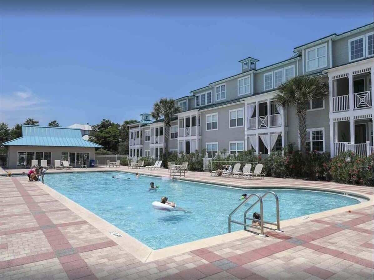 A swimming pool area with lounge chairs and a building with balconies.