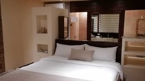 A bedroom with a large bed, a nightstand, a mirror, and a window with blinds. - Hotel Boutique Kpricho (SAN Antonio de las Minas)