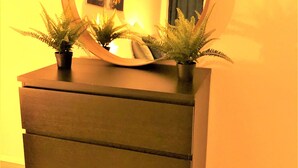 Une commode surmontée d’un miroir rond et de deux plantes en pot.