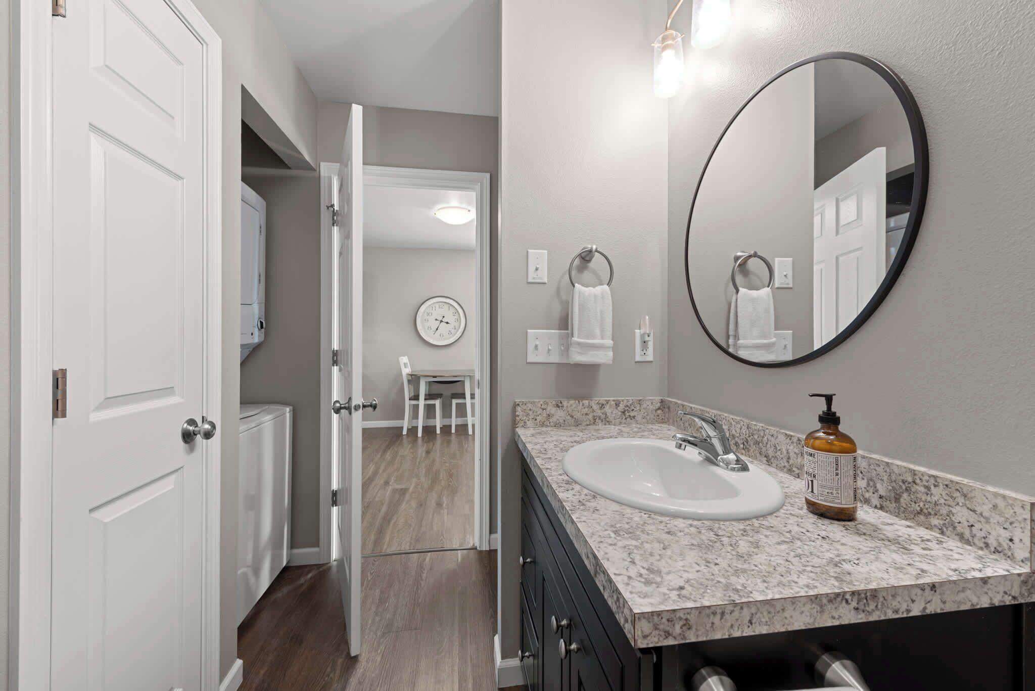A bathroom with a white sink, a round mirror, and a bottle of hand soap on the counter.