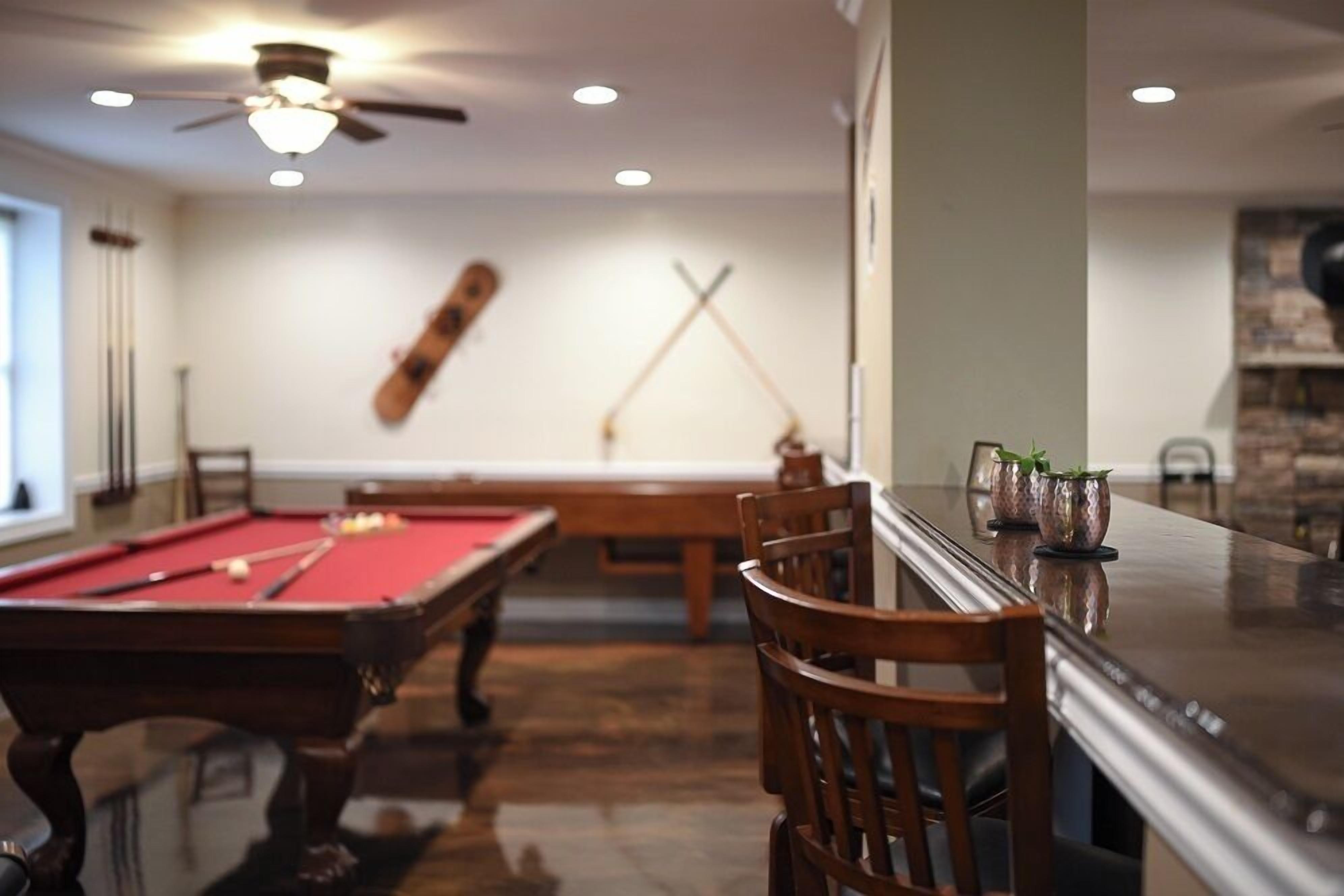 Une table de billard avec des chaises, une table de jeu de pool et un coin bar avec des tabourets.