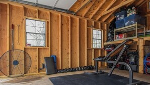 Uma academia com paredes de madeira, um ventilador, halteres e equipamentos de exercícios.