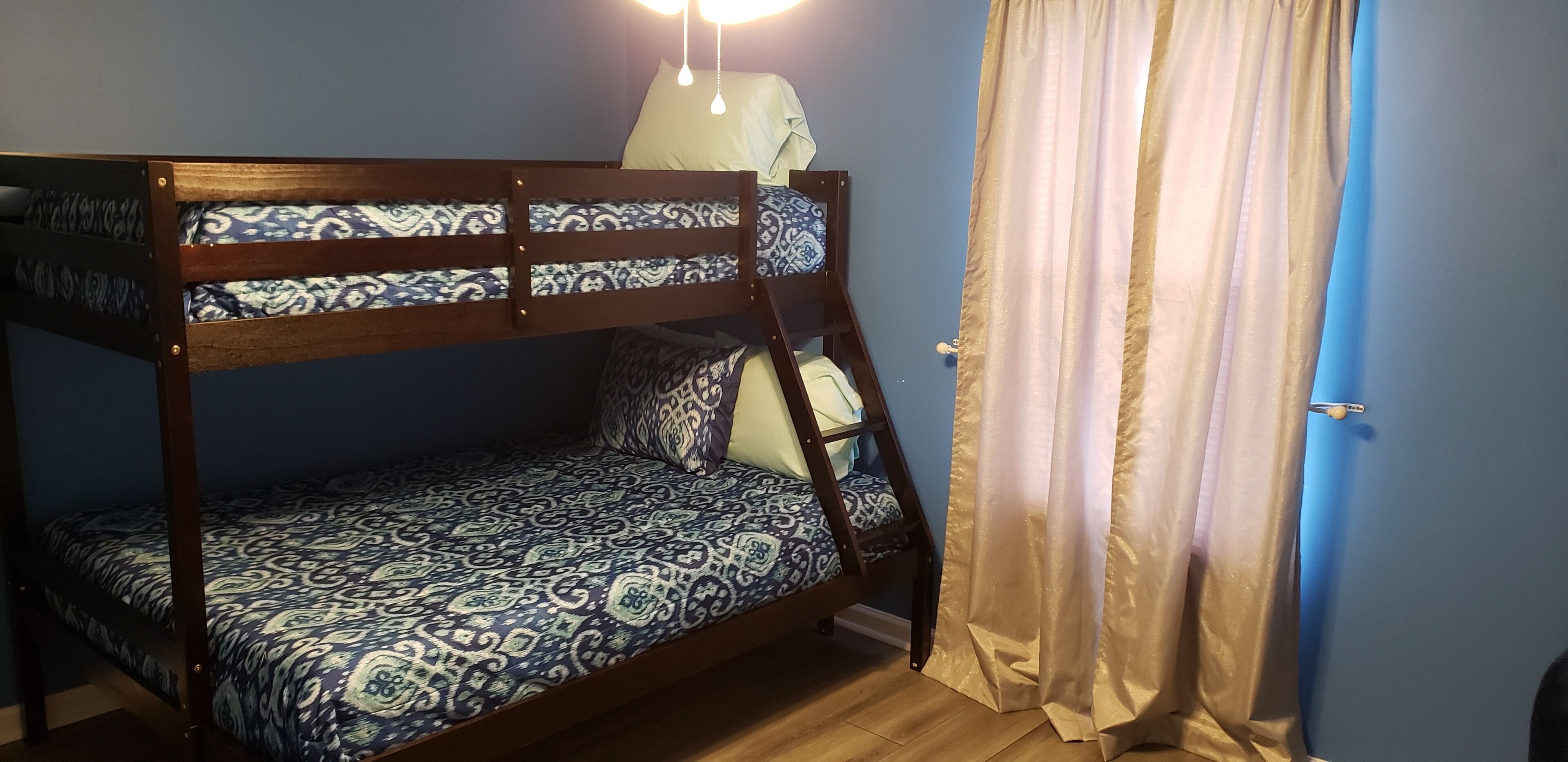 A bunk bed with patterned bedding, a bedside table, and a curtain.