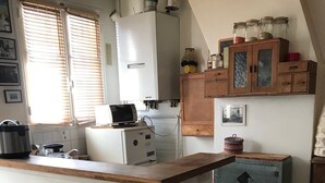 Eine Küche mit Holzausziehtisch, zwei Barhocker, einem weißen Kühlschrank, einem Herd und einem Fenster mit Jalousien.