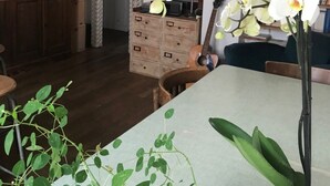 Ein Zimmer mit einem Holztisch, einem Bücherregal voller Bücher, einer Topforchidee und einem gemusterten Vorhang.