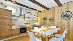 A modern kitchen with wooden cabinetry, a built-in oven, and a dining area with a white table and chairs. - Cozy home in Mrzlo Polje with sauna (Mrzlo Polje)
