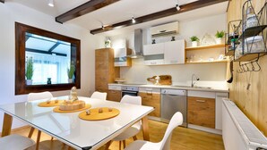 A modern kitchen with white cabinetry, a glass dining table, and a wooden floor. - Cozy home in Mrzlo Polje with sauna (Mrzlo Polje)