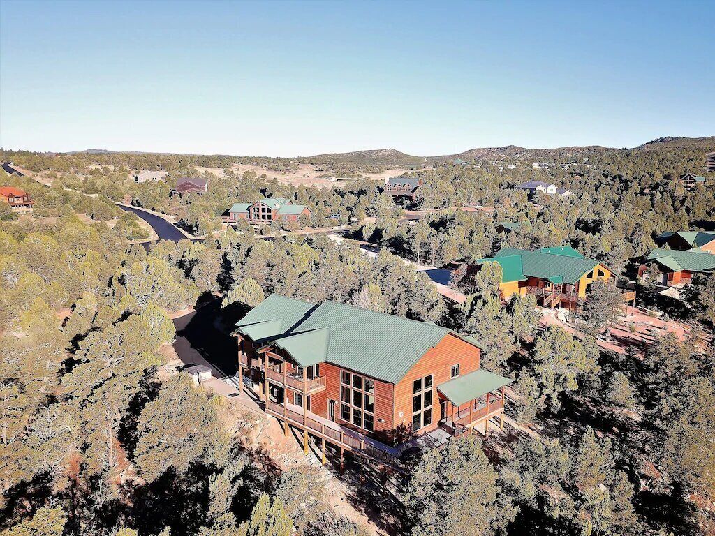 A large lodge with multiple guest rooms, surrounded by dense forest and hills.